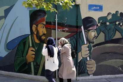 Mujeres iraníes pasan junto a un dibujo callejero de soldados en Teherán.