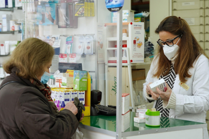 Una farmacéutica atiende a una cliente, ambas con mascarilla, el 8 de enero de 2024. EFE/Nacho Gallego