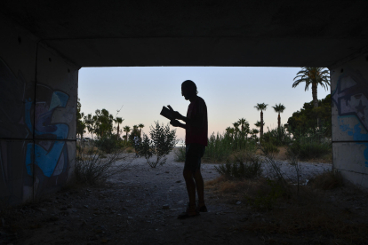 Miguel Rosa, natural de Córdoba, lee un libro bajo el puente en el que reside en Roquetas de Mar (Almería) y desde donde desarrolla su pasión que es escribir, un hombre sin techo que llegó a esta provincia para ganarse la vida bajo el plástico de los invernaderos. EFE / Carlos Barba