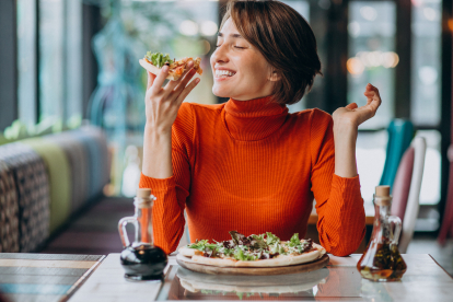 Mujer paladeando una pizza con ingredientes vegetales