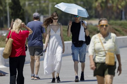 Una pareja utiliza una sobrilla para protegerse del sol este miércoles cuando el calor sofocante comienza a apretar. EFE/Ana Escobar
