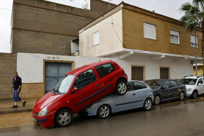 Una persona pasa junto a unos coches amontonados debido a las lluvias torrenciales que afectan a la Comunitat Valenciana, y especialmente a la provincia de Valencia, en la que se ha establecido el aviso rojo. EFE/Ana Escobar