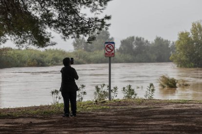 Una mujer toma imágenes del gran caudal del río Júcar a su paso por Albalat de la Ribera a causa de la dana que ha afectado a la provincia de Valencia.