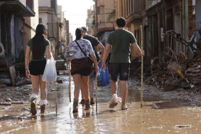 Varias personas caminan entre el lodo acumulado en las calles a causa de las intensas lluvias caídas por la fuerte dana, este jueves en Catarroja.