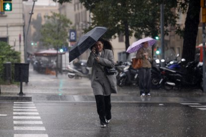 Una mujer se protege de la lluvia en el centro de Barcelona este lunes cuando las comarcas de del Garraf y del Barcelonès, en Barcelona, están en aviso rojo de la Agencia Estatal de Meteorología (Aemet), y la Generalitat ha enviado una alerta a los teléfonos móviles por la llegada de lluvias continuadas y torrenciales. EFE/Alberto Estévez