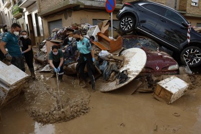 Los vecinos limpian las calles junto a varios coches apilados en Catarroja, Valencia este martes, una de las localidades más afectados por las inundaciones. EFE/ Chema Moya