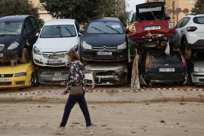 Una mujer pasa junto a decenas de coches que esperan ser retirados en Paiporta. EFE/Biel Aliño