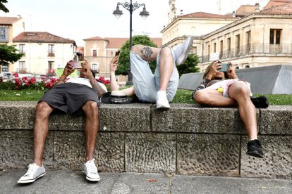 Tres jóvenes consultan el móvil tumbados en la calle en el centro de León.