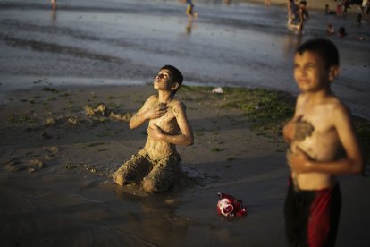 Un niño palestino cubre su cuerpo con arena como un tratamiento contra los hongos.