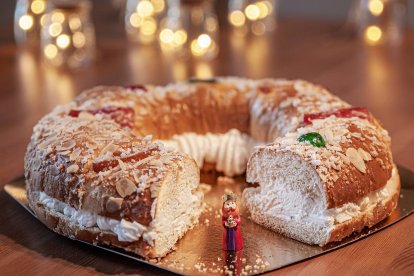 Detalle de un roscón de Reyes tradicional con nata, decorado con almendras y frutas confitadas, junto a la figura del rey escondida en su interior.