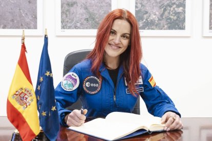 La astronauta Sara García‑Alonso firma el libro de visitas del SatCen vestida con su traje de la ESA, flanqueada por las banderas de España y la Unión Europea.