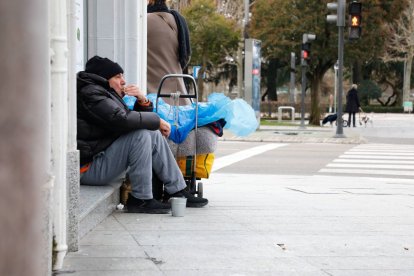 Un transeúnte, sentado en un umbral en una acera de León capital.