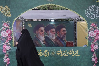 Una mujer vestida con el tradicional chador pasa delante de un cartel en Teherán que muestra a los tres líderes supremos.