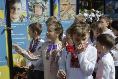 Niños ucranianos dejan flores ante los retratos de ucranianos asesinados por Rusia. SERGEY DOLZHENKO