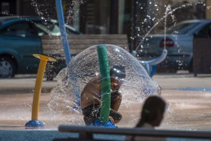 Un niño se refugia del calor debajo de una fuente