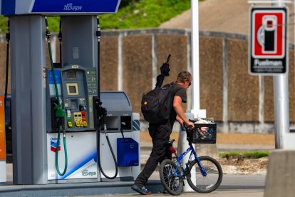 Un hombre pasa caminando con una bicicleta frente a una estación de servicio.