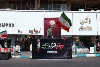 Un hombre iraní iza la bandera nacional en la Plaza Valiasr de Teherán.