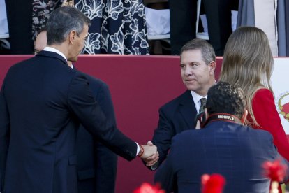 El presidente de Castilla-La Mancha, Emiliano García-Page (d), saluda al presidente del Gobierno, Pedro Sánchez (i), durante el tradicional desfile militar por las calles del centro de Madrid en el que participan casi 4.400 militares, 144 vehículos, 39 motos, 50 aviones y 32 helicópteros, este lunes Día de la Fiesta Nacional.- EFE/ Ballesteros.
