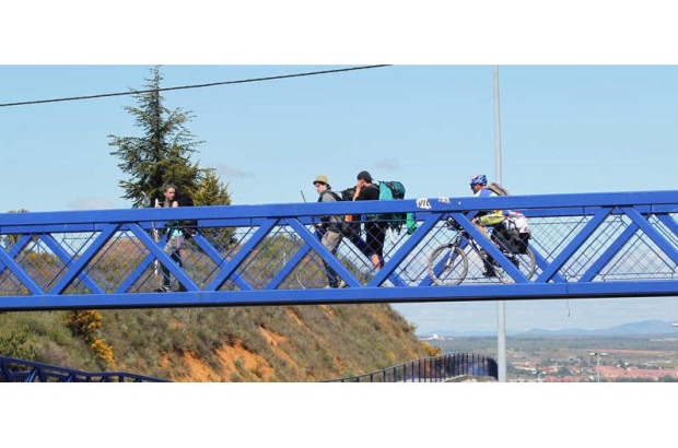 Peregrinos caminan por la pasarela del Alto del Portillo en su senda de entrada a la capital de la provincia.