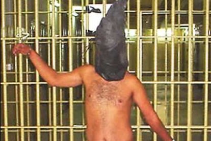 Un prisionero iraquí esposado desnudo a la puerta de una celda.