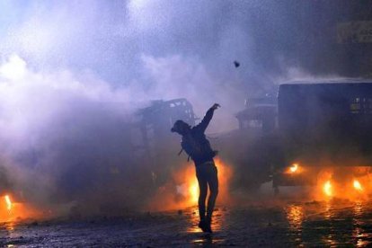 Un manifestante lanza una piedra durante los enfrentamientos con la policía en el centro de Kiev. La policía utilizó gases lacrimógenos y bolas de humo en un intento de dispersar a cientos de personas que trataron de romper un cordón policial junto a la sede del Gobierno. AFP PHOTO / SERGEI SUPINSKY