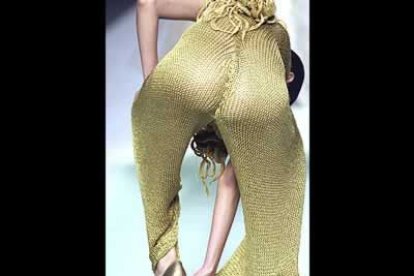 Una modelo intenta separar el tejido de rejilla dorada de su pantalón, del tacón de aguja con el que se había enredado, durante el desfile.