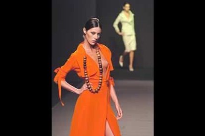 Vestido en seda naranja con anudados en las mangas, y abotonado central. Collar de bolas extremas.