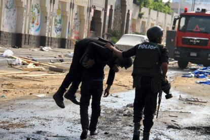 Dos policías antidisturbios retiran a un compañero herido durante los enfrentamientos. AP / AHMED GOMAA