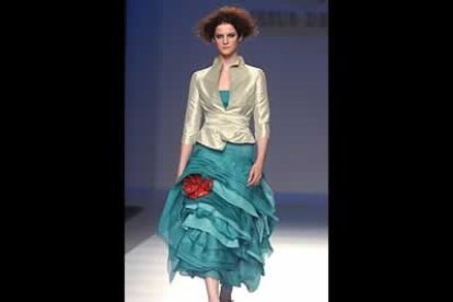 Chaqueta anudada a la cintura en un tono camel brillante. El vestido con volantes y pliegues al biés. La tona de color el detalle de la flor y los zapatos en rojo intenso.