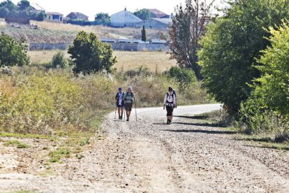 La iglesia de Valdelafuente y vista del pueblo de Arcahueja. Abajo, unos peregrinos surcan este tramo del Camino.