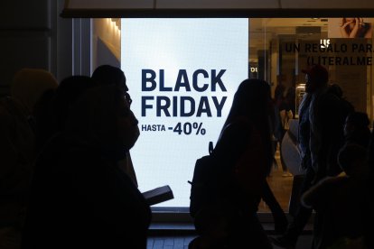Peatones pasan por delante del escaparate de un comercio madrileño que anuncia rebajas por el 'Black Friday'. EFE/ Juanjo Martín