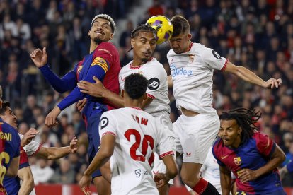 El defensa del Sevilla Loïc Badé (c) disputa un balón con el defensa del FC Barcelona Ronald Araújo (i) durante un encuentro correspondiente a la jornada 23 de LaLiga EA Sports entre el Sevilla FC y el FC Barcelona en el estadioo Ramón Sánchez-Pizjuán de Sevilla. EFE/ Julio Muñoz
