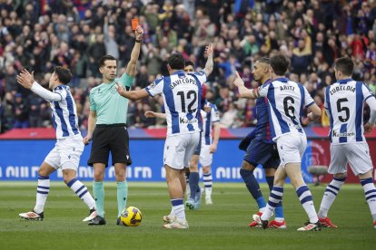El colegiado Alejandro Quintero González (2i) muestra tarjeta roja al defensa de la Real Sociedad Aritz Elustondo (2d) durante el partido de LaLiga EA Sports entre FC Barcelona y Real Sociedad, este domingo en el estadio Olímpico de Montjuic de Barcelona. EFE/ Andreu Dalmau