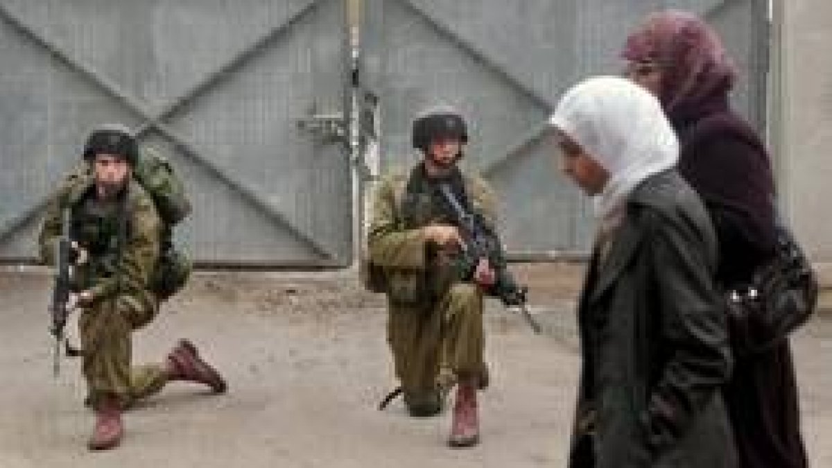 Dos mujeres palestinas pasan por delante de un soldado hebreo