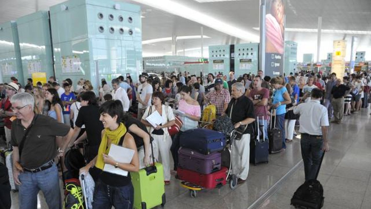Pasajeros hacen cola para facturar las maletas que no pueden embarcar como equipaje de mano, en el aeropuerto de El Prat.