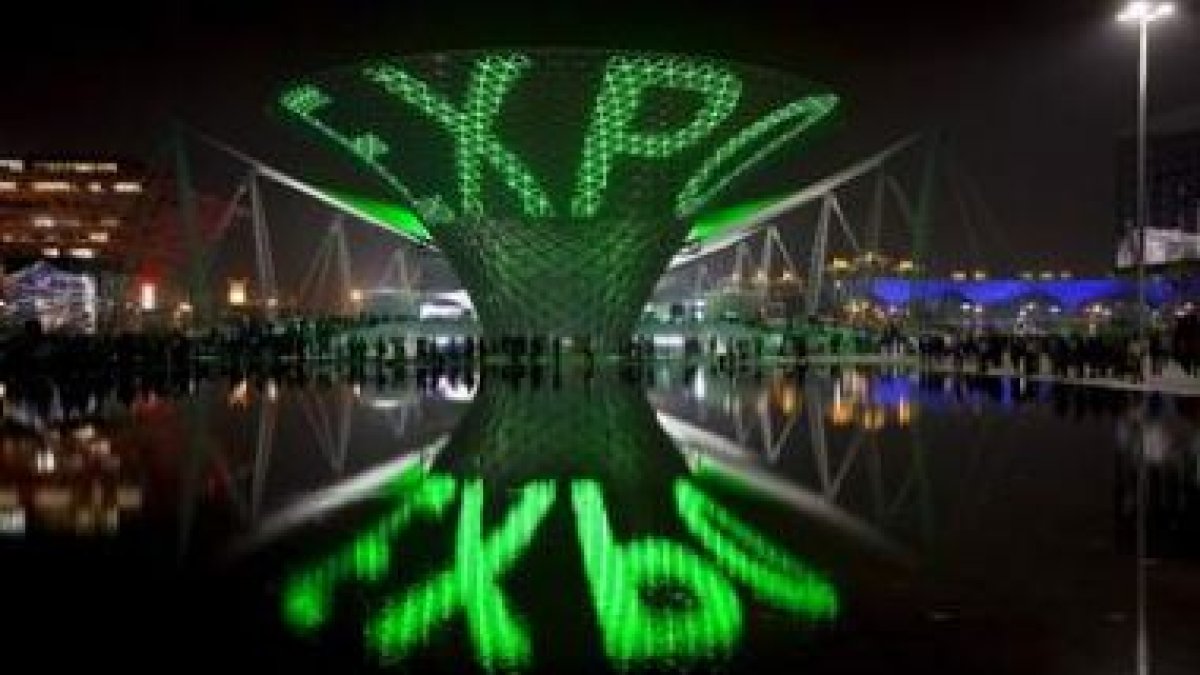 Imagen de uno de los edificios de la Expo iluminado que se refleja en un estanque.