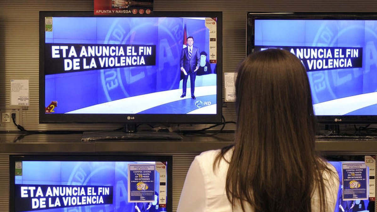 Una mujer observa los informativos en las televisiones de un centro comercial.