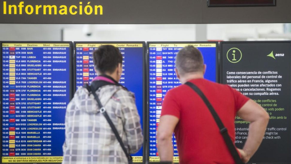 Dos viajeros observan el panel de salidas en el aeropuerto de El Prat, en plena huelga de controladores en Francia.