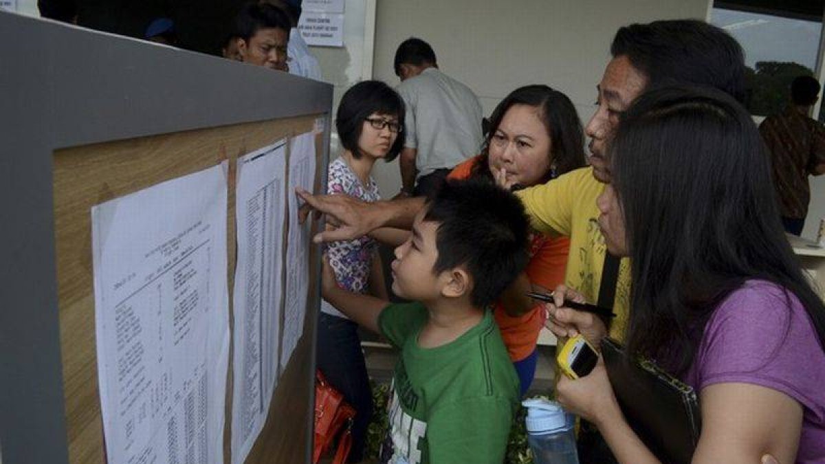 Familiares de los pasajeros del vuelo desaparecido miran una lista en el aeropuerto de Surabaya, este domingo.