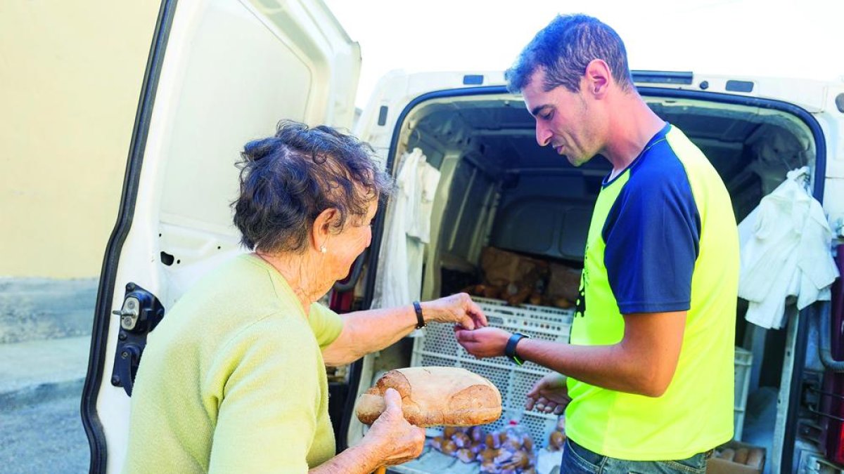 El repartidor Roberto Corral reparte una barra de pan a una vecina de Villafañe.