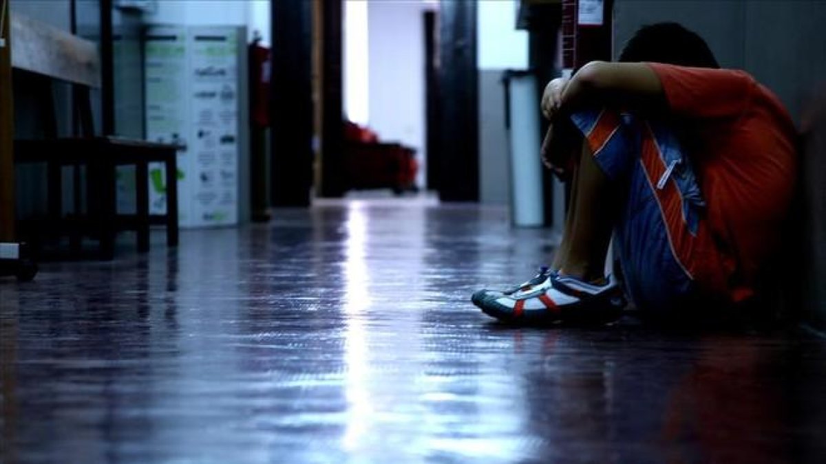Un adolescente se oculta la cara sentado en el pasillo de su instituto.