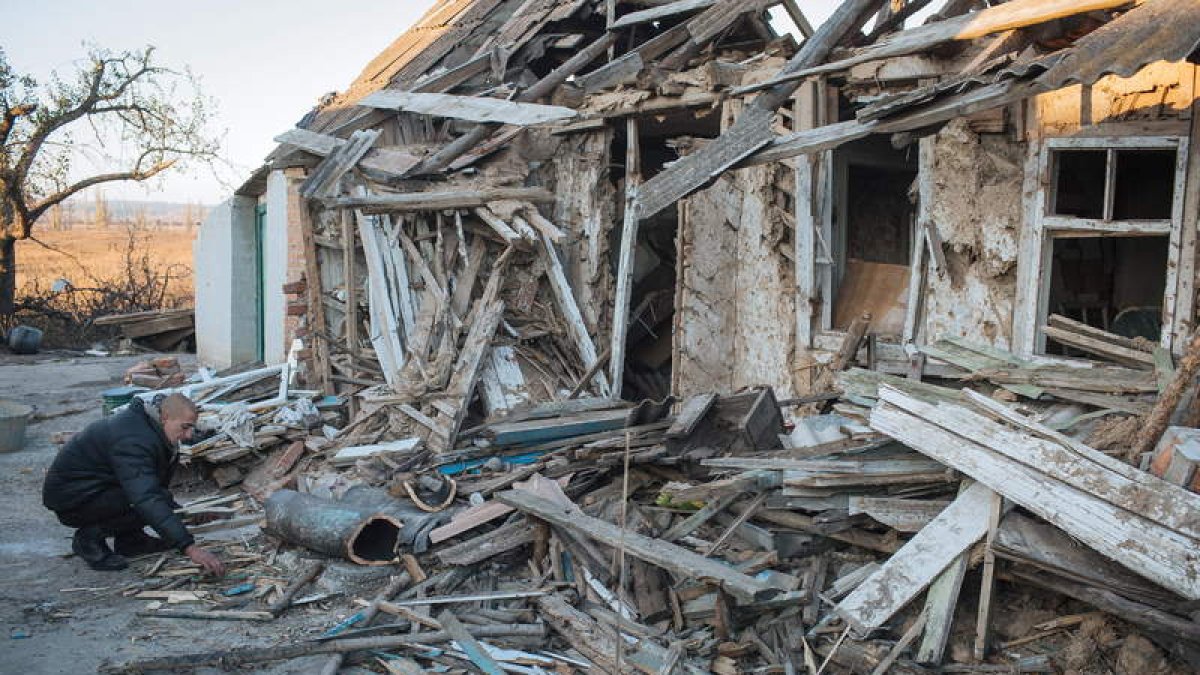 Un hombre recoge restos de madera junto a su casa destruida por los combates.