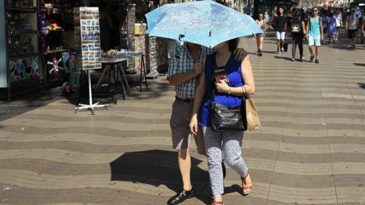 Ola de calor en Barcelona. Una pareja se protege del sol con un paraguas en las Ramblas.