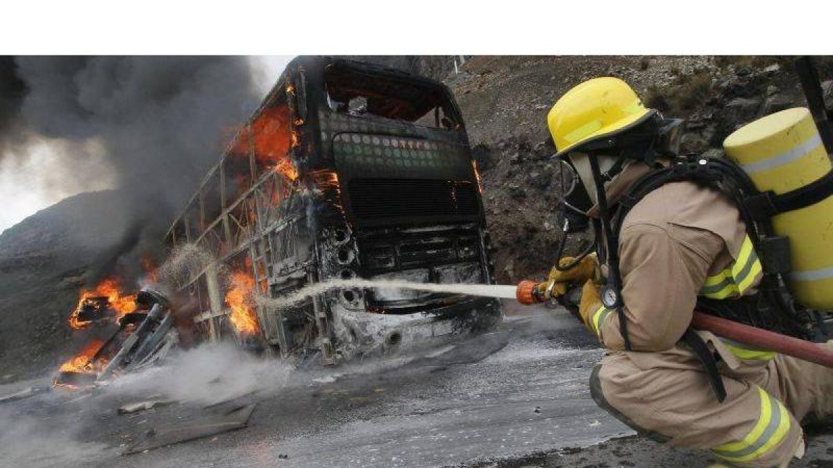 Un bombero trata de extinguir el fuego de un autobús en llamas.