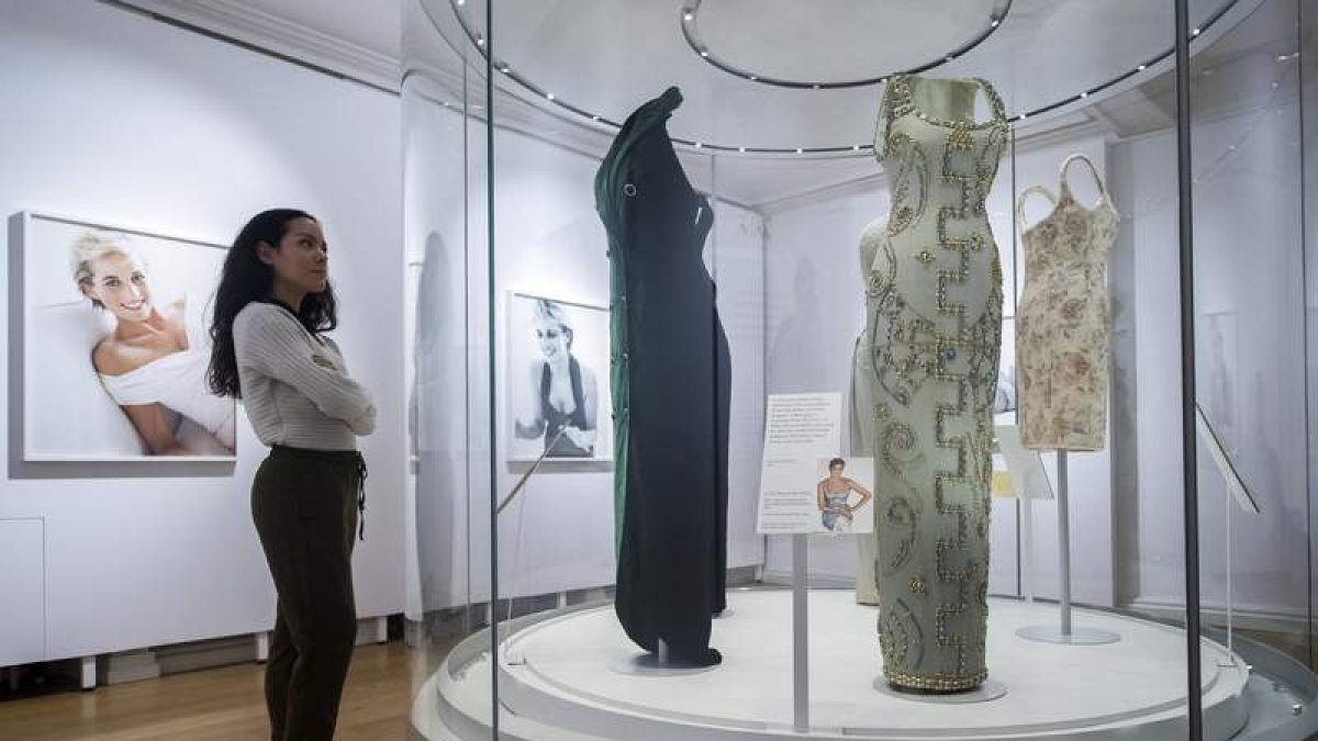 Una empleada posa junto a varias fotografías y algunos de los vestidos de la princesa Diana de Gales. WILL OLIVER
