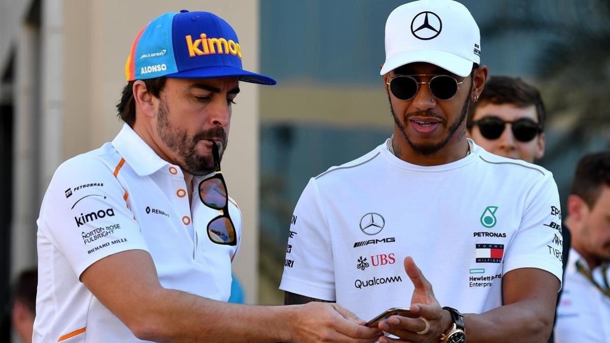 Alonso consulta un móvil junto a Hamilton en Abu Dhabi.