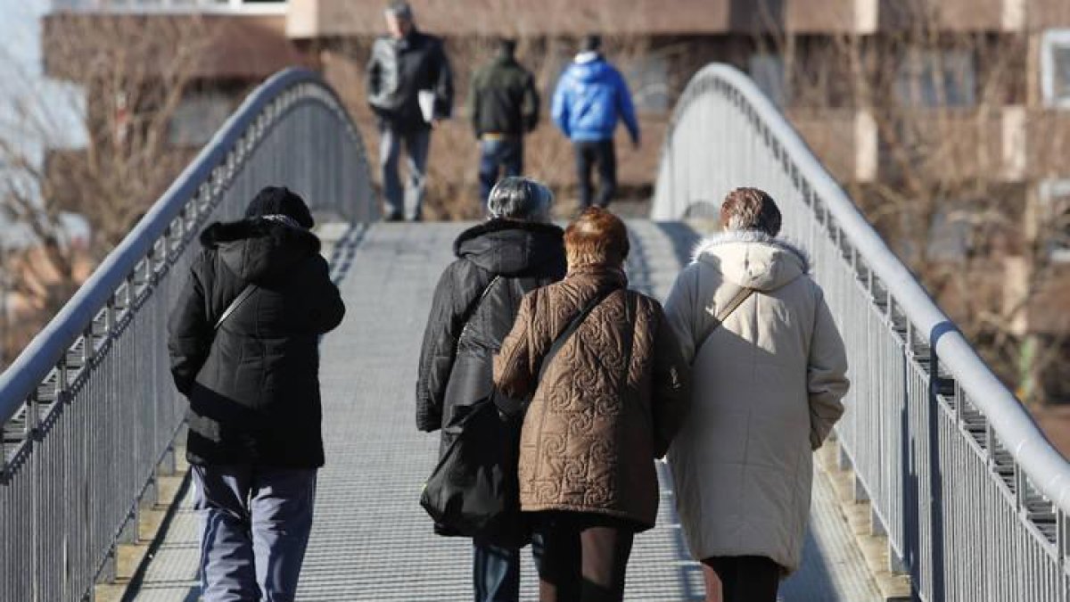 Varias personas mayores cruzan uno de los puentes peatonales sobre el Bernesga.