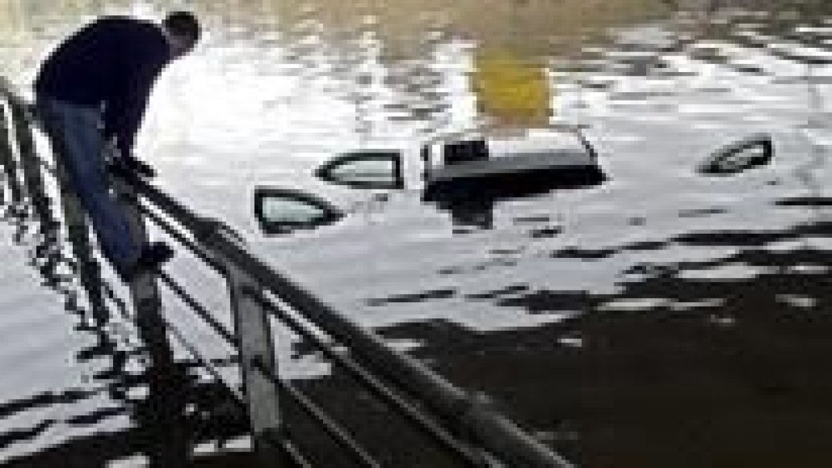 Una persona intenta cruzar un puente, mientras que un taxi permanece cubierto por la tromba