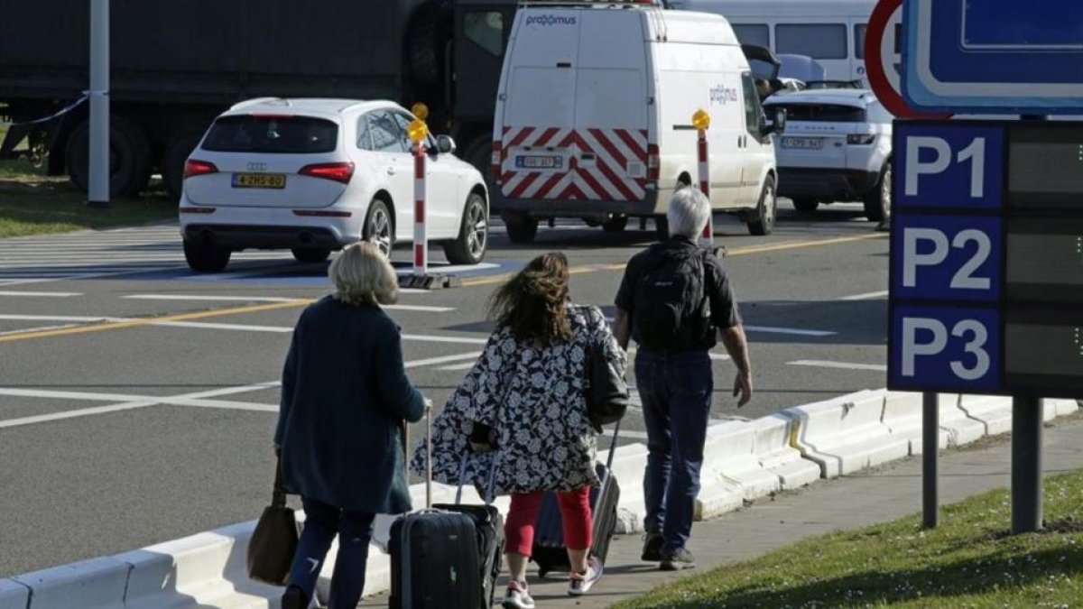 Varias personas caminan hacia la terminal mientras los vehículos hacen cola en un control de seguridad, en el aeropuerto de Zaventem, este lunes.