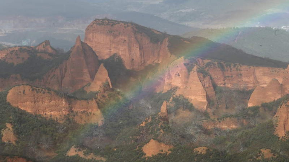 El arco iris en Las Médulas, visible desde el mirador de Orellán, con los picachos de arcilla rodeados de castaños y al fondo a la izquierda la sombra de la cantera de Peña El Rego, ya sin actividad.